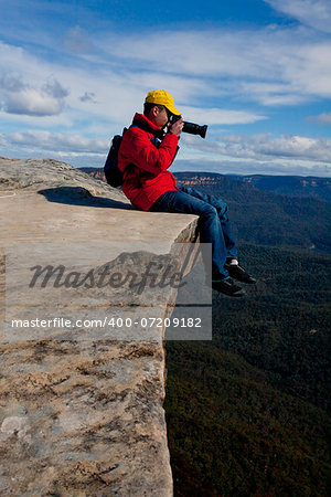 Tourist or photographer on a cliff edge taking photos  of a mountainous landscape