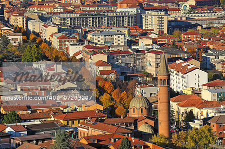 Urban buildings with red roofs and church lit by last rays of setting sun at evening in Alba, Italy (view from above).