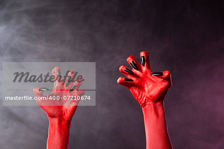 Spooky red devil hands with black glossy nails, Halloween theme, studio shot over smoky background
