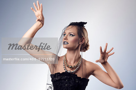 portrait of attractive blonde girl with goth style in the halloween day in aggressive pose. She wearing dark veil on the face, black corset and creative make-up