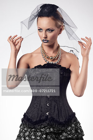 fashion blonde woman with gothic bizarre halloween costume and creative make-up posing with dark veil on the hand and sexy corset