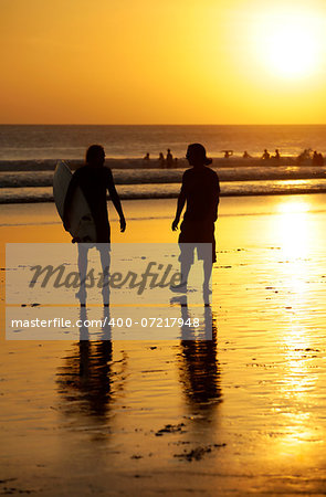 Silhouette of surfers in golden sunset light. Bali