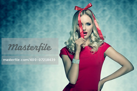 christmas shoot of beauty blonde elegant woman with red fashion dress and bright bracelet posing with funny bow on her head like a present