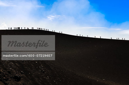 Group of trekkers hiking on a volcano hill with blue sky background