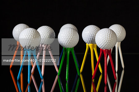 White golf balls and different colored tees on a black desk