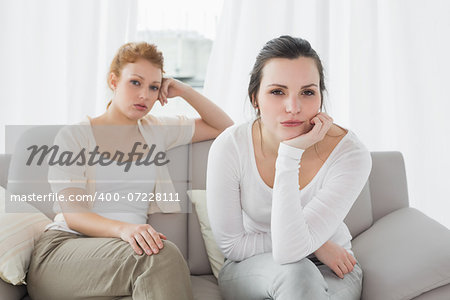 Unhappy young female friends not talking after argument at home on the couch