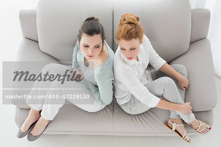 High angle view of unhappy young female friends not talking after argument at home on the couch