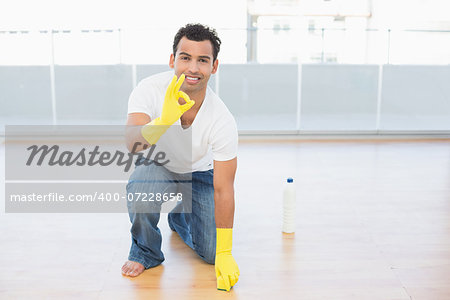 Portrait of a smiling young man cleaning the floor while gesturing okay sign at house