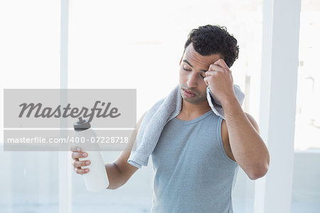 Tired young man wiping sweat with towel in a bright fitness studio