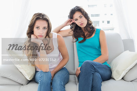 Portrait of unhappy young female friends not talking after argument at home on the couch