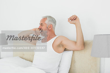 Mature man waking up in bed and stretching his arms at home