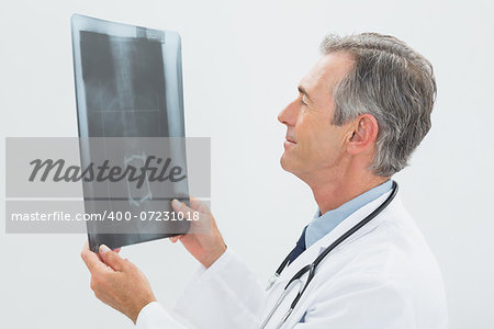 Side view of a concentrated male doctor looking at x-ray over white background