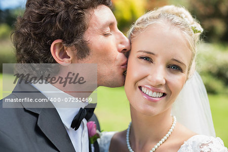 Groom kissing his pretty blonde wife on the cheek in the countryside