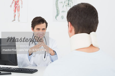 Smiling male doctor in conversation with patient at desk in medical office