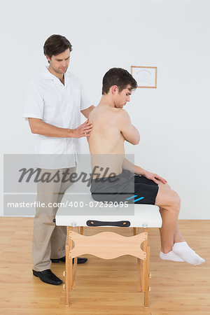 Side view of a shirtless man being examined by a physiotherapist in the medical office