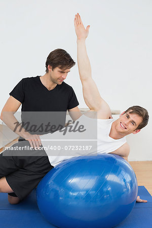 Physical therapist assisting young man with yoga ball in the gym at hospital