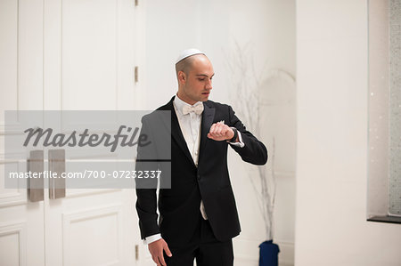 Anxious, Jewish Bridegroom standing in front of temple doors, looking at watch on Wedding Day, Canada