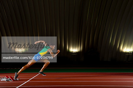 Young woman sprinting from starting blocks in stadium