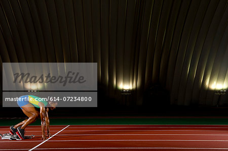 Young woman sprinting on starting blocks in stadium