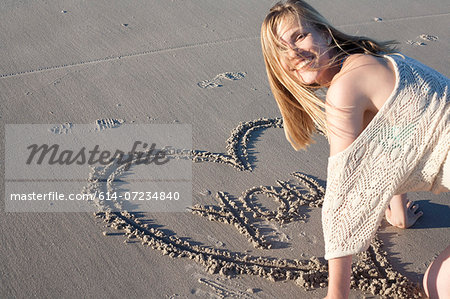 Smiling woman writing love message in sand, Breezy Point, Queens, New York, USA