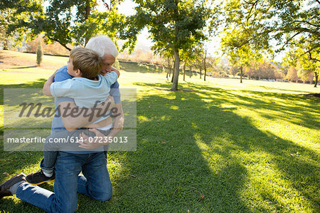 Grandfather kneeling on grass hugging grandson