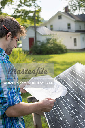 A man using a plan to place a solar panel in a farmhouse garden.