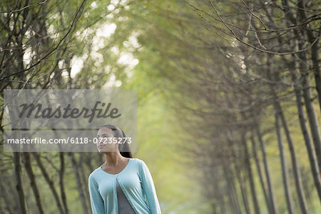 A woman between two rows of trees, looking upwards.