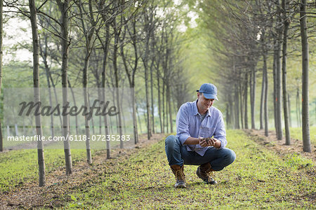 A man crouching and examining a handful of soil.