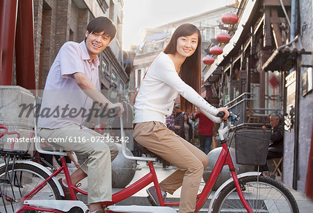 Side View of Young Heterosexual Couple on a Tandem Bicycle in Beijing Looking at Camera