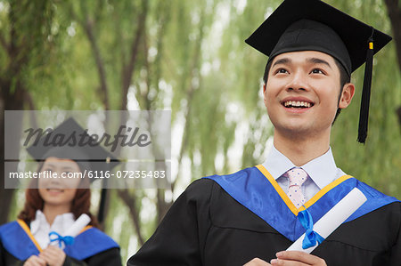 Two Young University Graduates Holding Diplomas, Man in Front