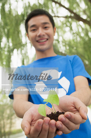 Young Man Holding Seedling in his Hands, Recycling Symbol, Low Angle View