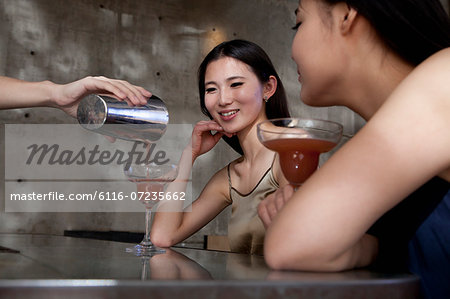 Young women having cocktails, sitting at the bar counter