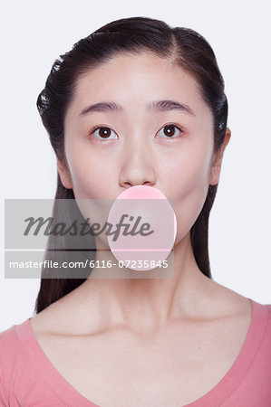 Young playful woman blowing a bubble out of bubble gum, studio shot