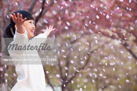 Happy young girl throwing cherry blossom petals in the air outside in a park in springtime