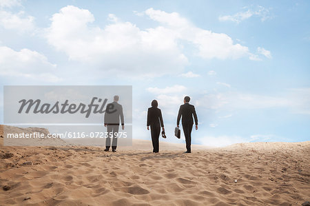 Three young business people walking through the desert, rear view, distant