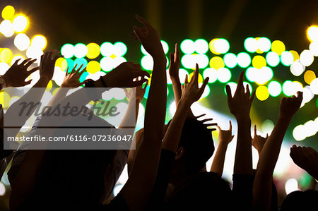 Audience watching a rock show, hands in the air, rear view, stage lights