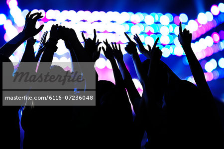 Audience watching a rock show, hands in the air, rear view, stage lights