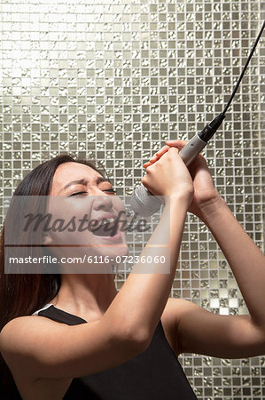 Young woman singing into a microphone at karaoke, shiny background
