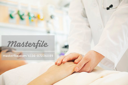 Close up of doctor holding a patients hands lying down on a hospital bed