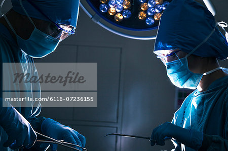 Two surgeons looking down and working at the operating table, dark operating room