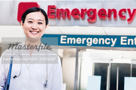 Portrait of smiling female doctor outside of the hospital, emergency room sign in the background