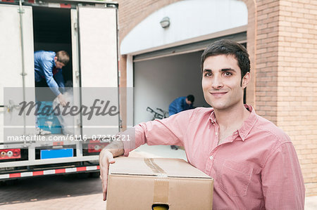 Smiling man holding a cardboard box and moving into his new home