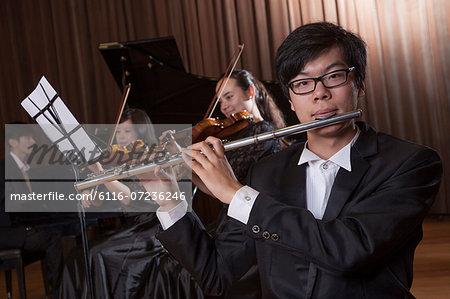 Flautist holding and playing the flute during a performance, looking at the camera