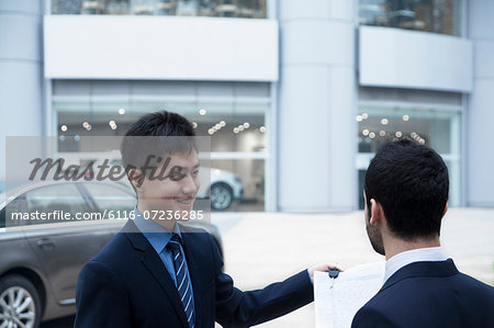 Car salesman holding car keys and paperwork and selling a car to a young businessman