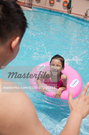 Little girl with a pink tube and her father swimming in the pool