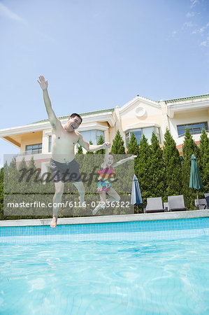 Father and daughter holding hands and jumping into the pool