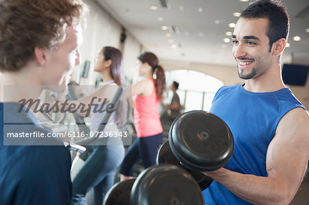 Two young men smiling and lifting weights in the gym