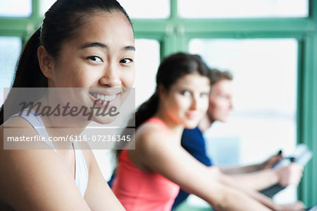 Young women exercising on fitness bikes in the gym, looking at camera