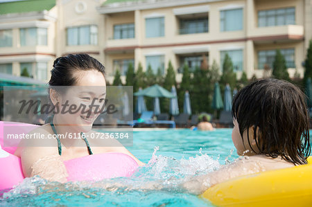 Smiling mother and son floating on inflatable tubes and playing in the pool
