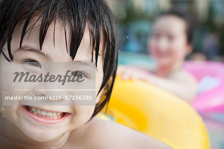 Portrait of smiling boy in the pool on a an inflatable tube with his mother in the background